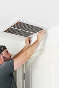 man opening return air vent in ceiling