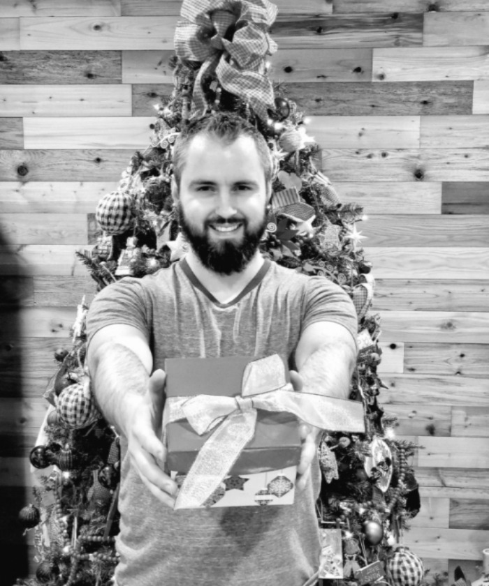 What not to buy your wife for Christmas. Man holding gift in front of Christmas tree.