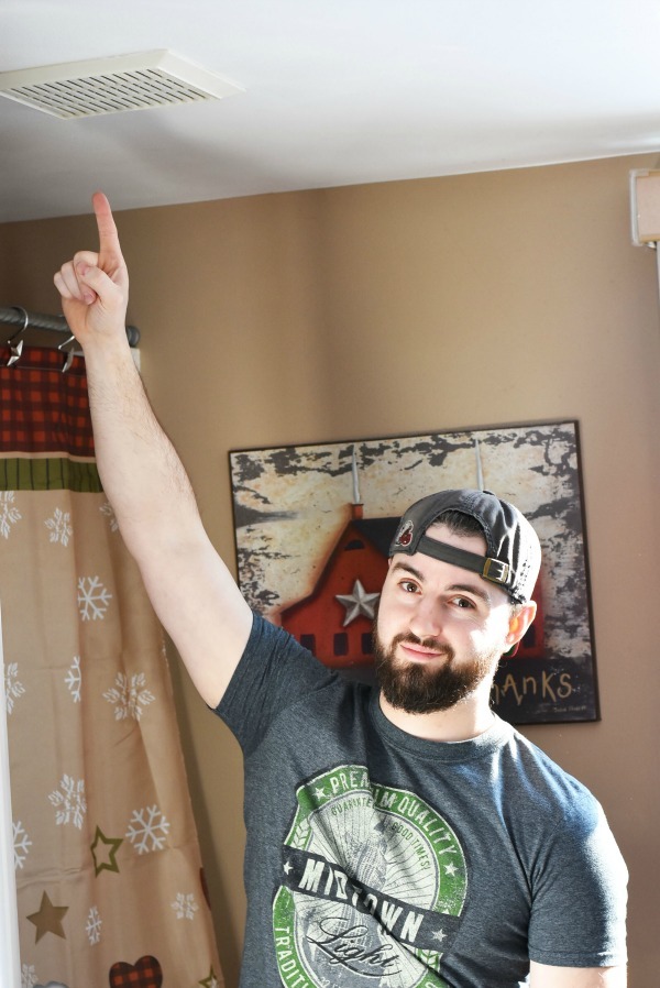 man pointing to old small bathroom exhaust fan in ceiling 