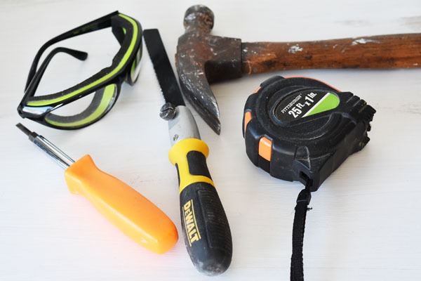 screwdriver, safety glasses, drywall saw, tape measure, and claw hammer on table
