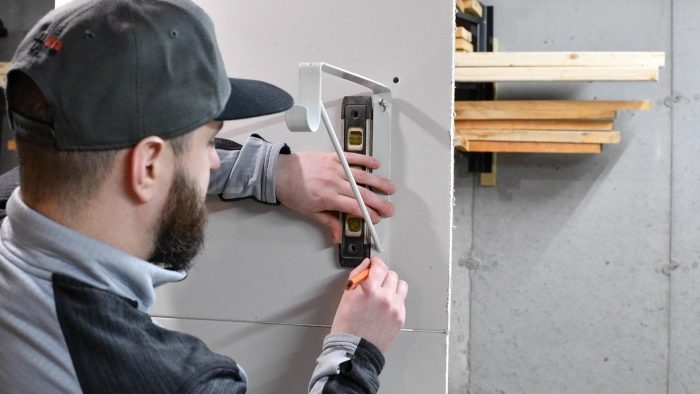 man holding a level to the side of a shelf bracket on the wall to level it. 