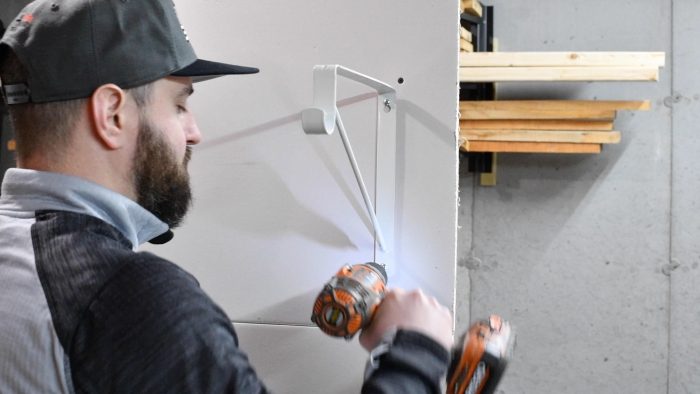 man screwing in a shelf bracket to a wall