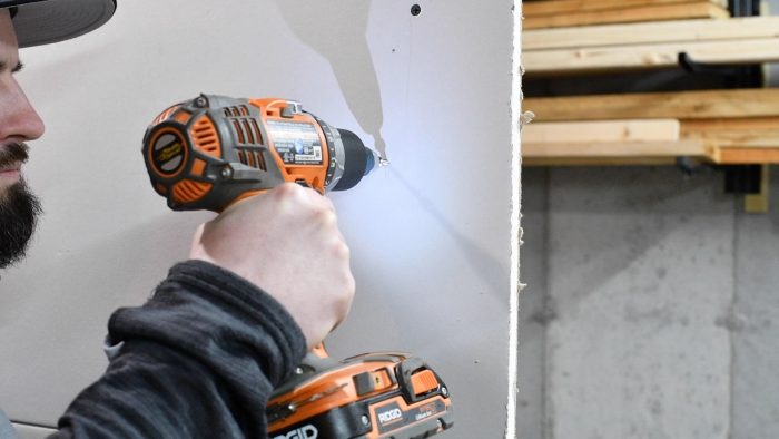 man screwing a screw into a wall with a hand drill