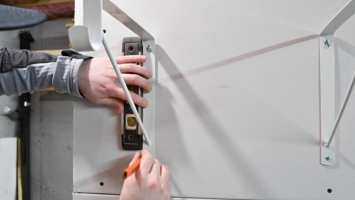 Man holding a level against the side of a shelf bracket and marking the bottom hole with a pencil.