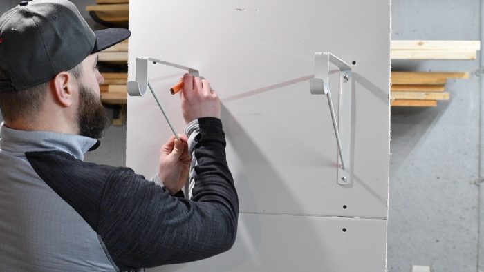 man marking the hole of a shelf bracket to the wall with a pencil