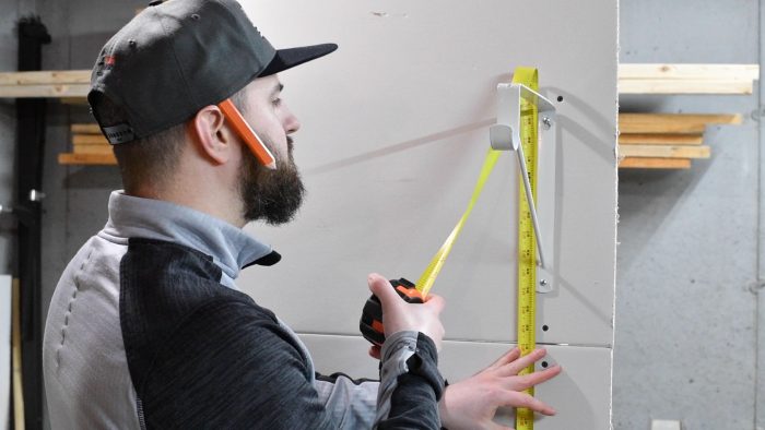 man measuring the top of a shelf bracket from the floor with a tape measure