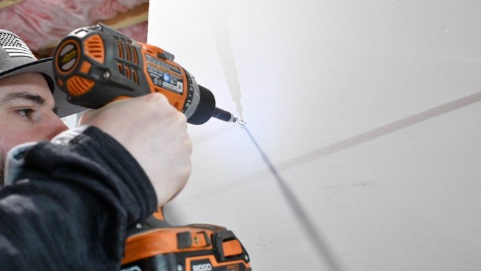 hand drill screwing a screw into a wall anchor