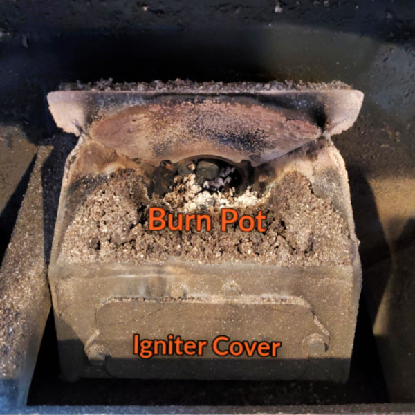 image of a pellet stove burn pot and the igniter cover below. Ash is inside the burn pot