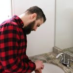 man sticking drain cleaning tool into bathroom sink drain