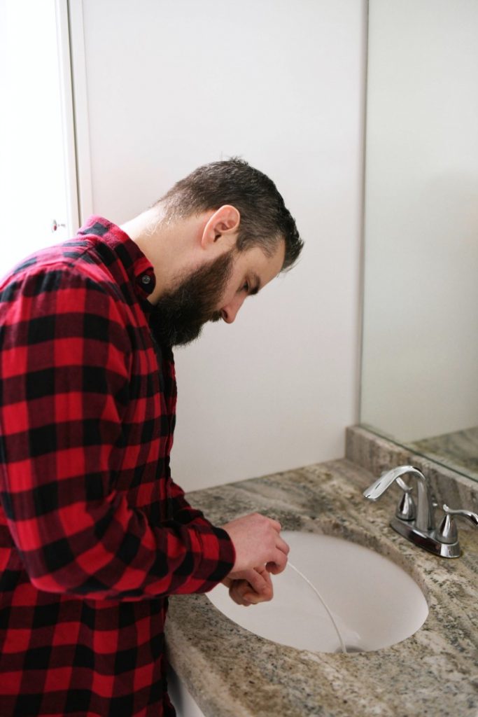 man sticking drain cleaning tool into bathroom sink drain