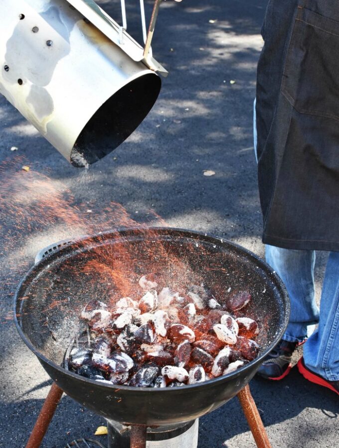 dumping burning charcoal into grill. Fire is seen coming off of glowing briquettes.