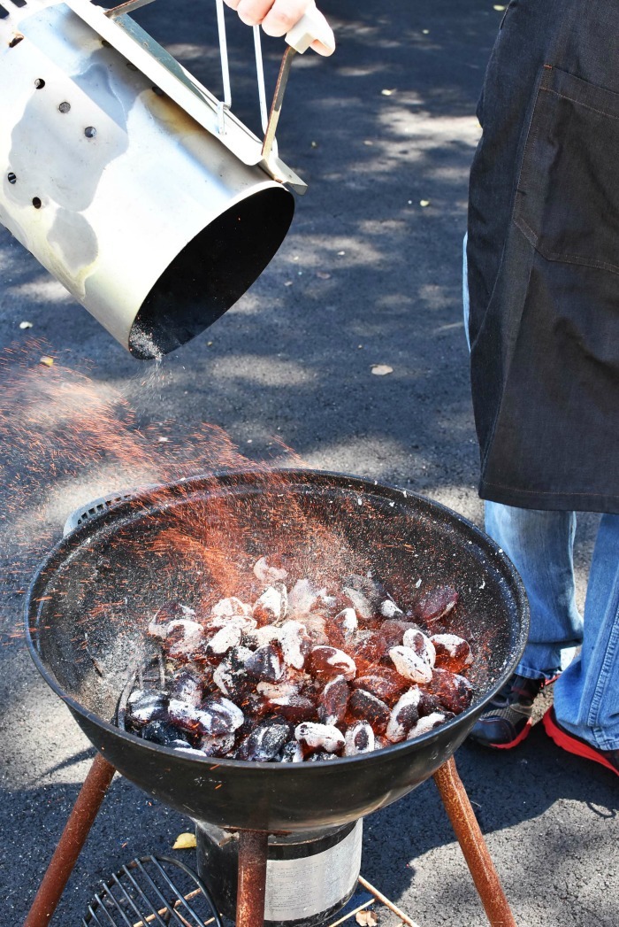 dumping burning charcoal into grill. Fire is seen coming off of glowing briquettes.