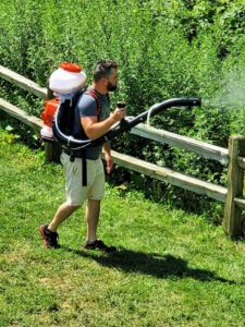 man spraying mosquito control mist into woods